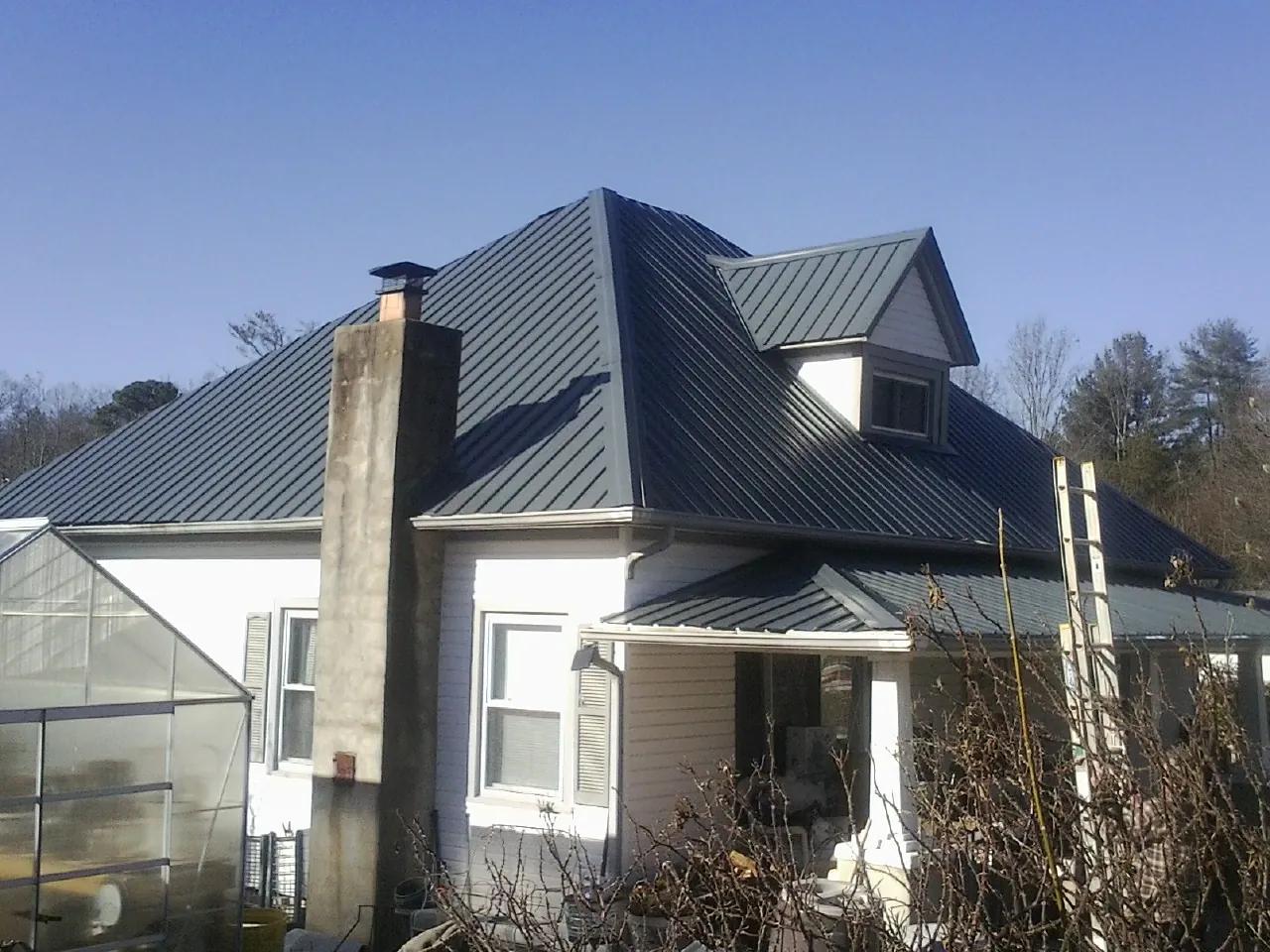 Dark blue standing seam metal roof on a white farmhouse with dormer — Slate & Tile Roof Repair by Roofing Brothers in Maury