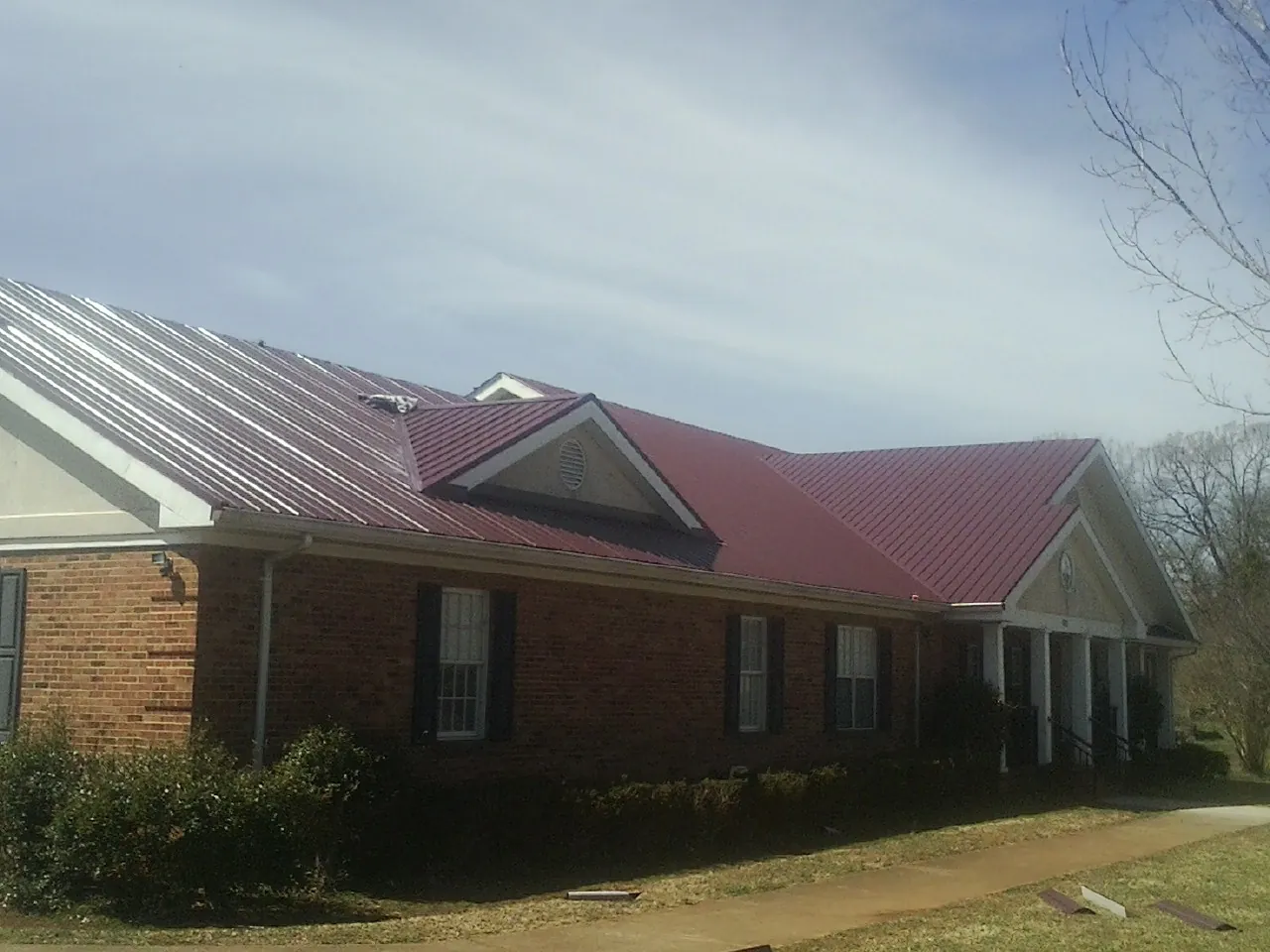 Red metal roof with gabled entries on a long brick building, from a Hail Damage Roof Repair job in Maury