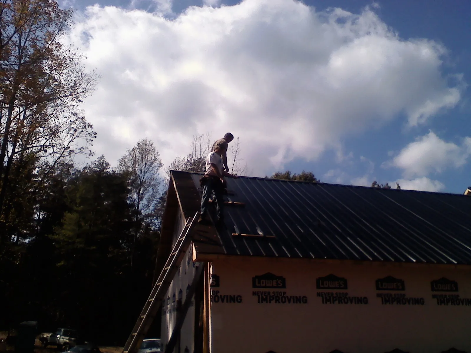 Roofer fastening dark metal panels high against a cloudy sky, from a Roof Inspection job in Maury