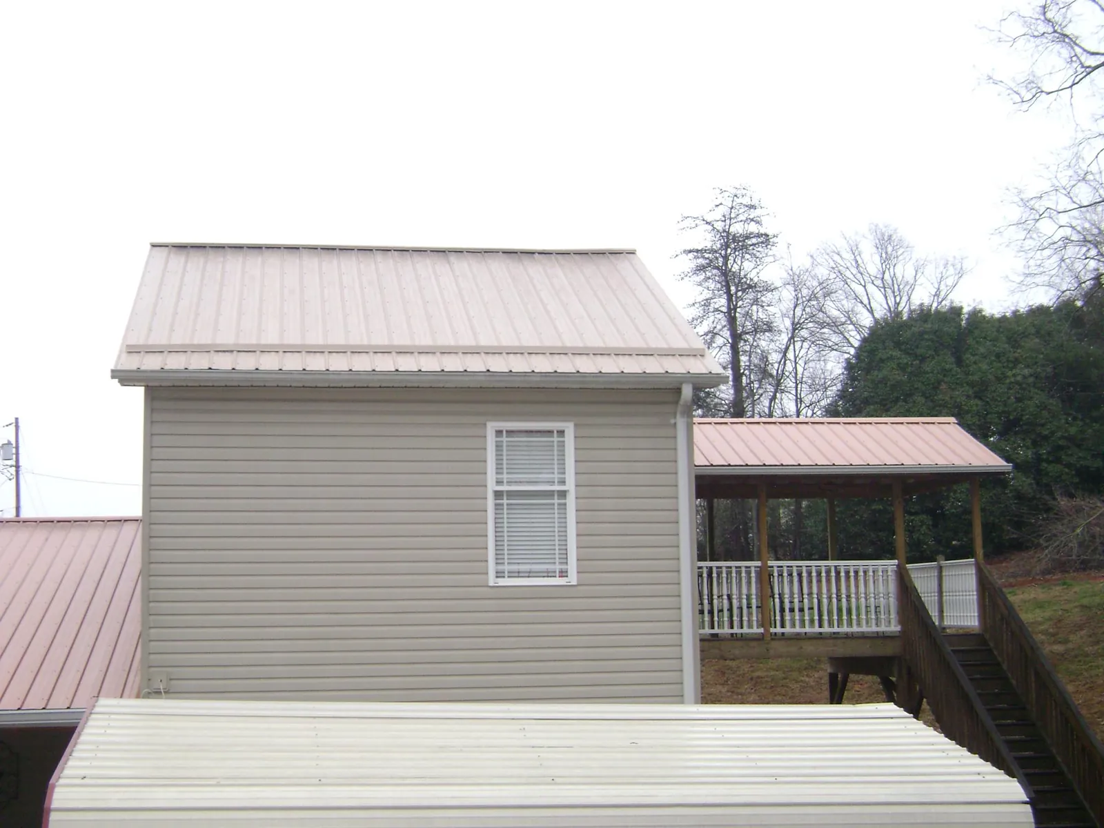 Tan metal roofs on a two story addition and attached porch, from a Roof Replacement job in Maury